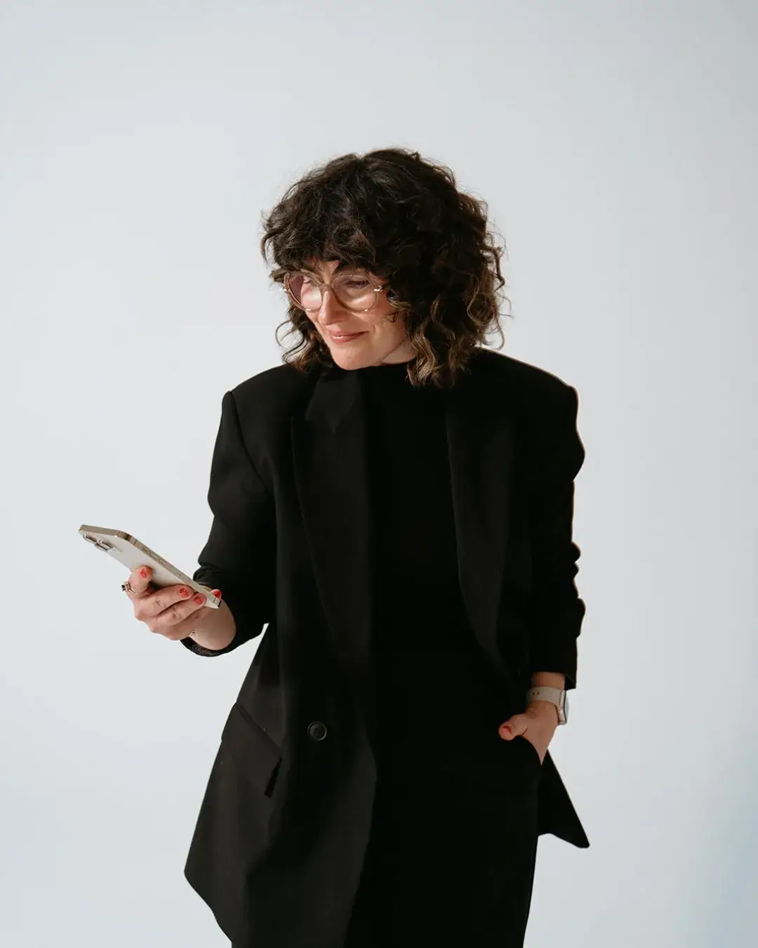 Sylvie Patten, wedding content creator based in France, smiling at her phone in a black blazer against a light grey background - Sparkly Studio